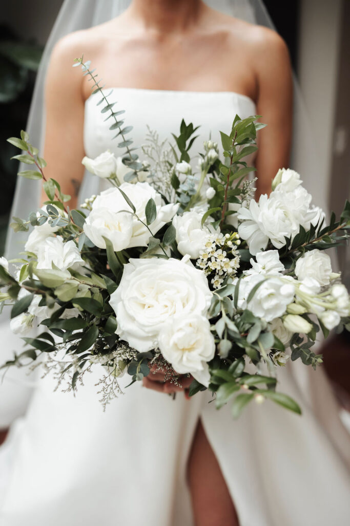 Bride holding a lush white and green wedding bouquet with roses, eucalyptus and mixed greenery.