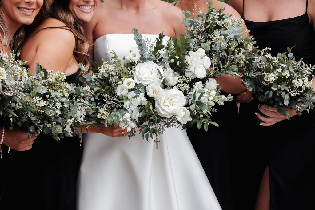 Bride and bridesmaids holding coordinated white and green bouquets with eucalyptus and mixed greenery.