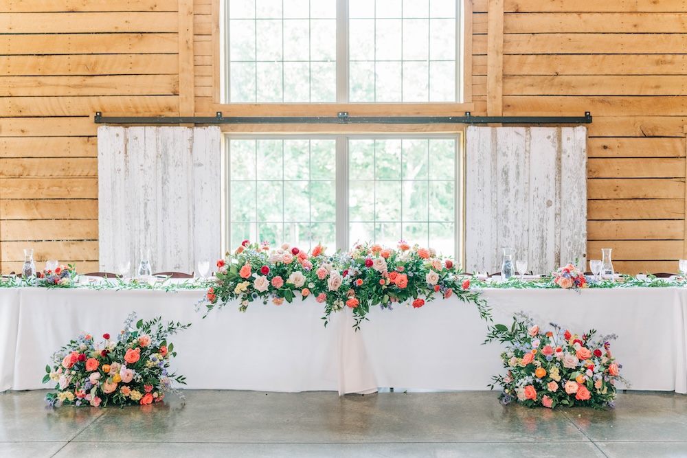 Colorful wedding flowers in coral, pink, blue and peach arranged across a long reception head table.