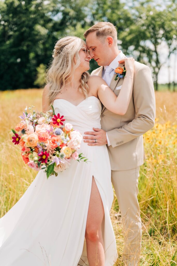 Bride and groom posing outdoors with a colorful garden-style wedding bouquet.