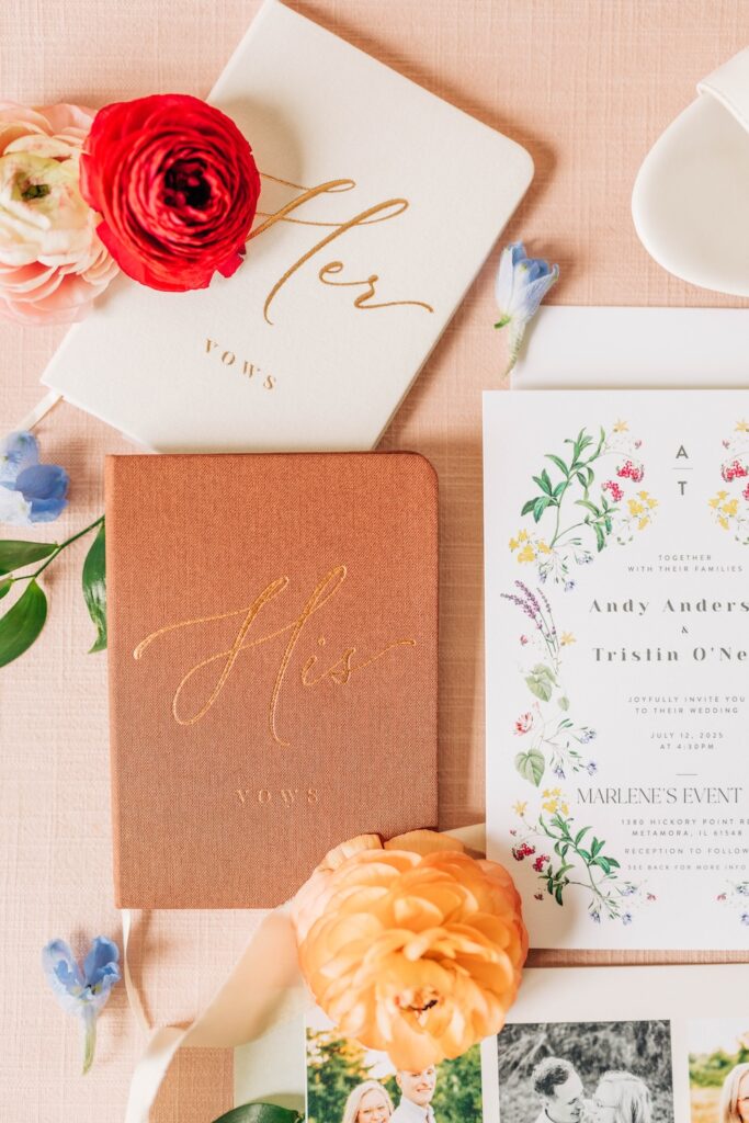 Wedding vow books and floral invitation suite styled with colorful ranunculus and blue flowers.