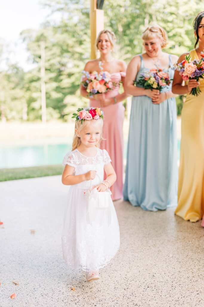 Flower girl wearing a floral crown with bridesmaids holding colorful bouquets behind her.