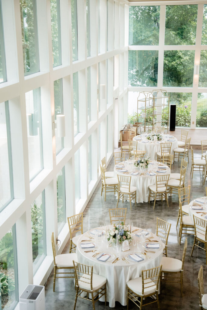 Bright wedding reception space with round tables, gold chairs and low pastel floral centerpieces.