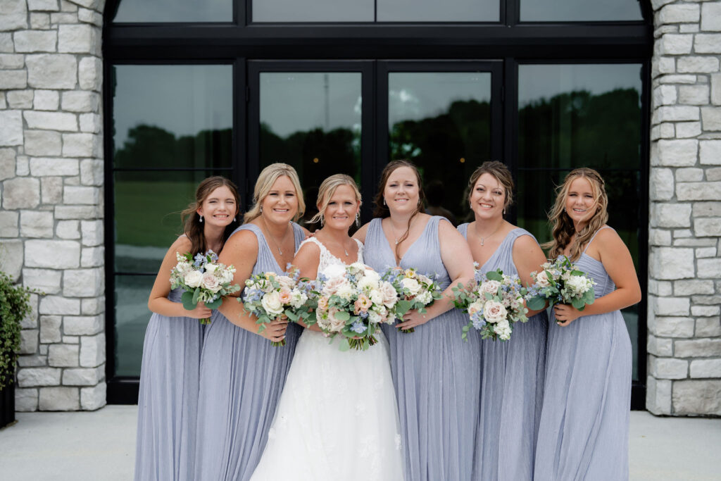 Bride with bridesmaids in dusty blue dresses holding white, blush and blue wedding bouquets.