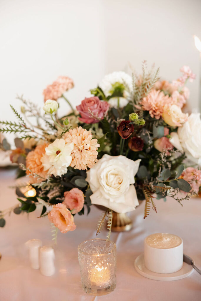 Close-up of a wedding centerpiece with peach, blush, burgundy and white flowers with greenery.