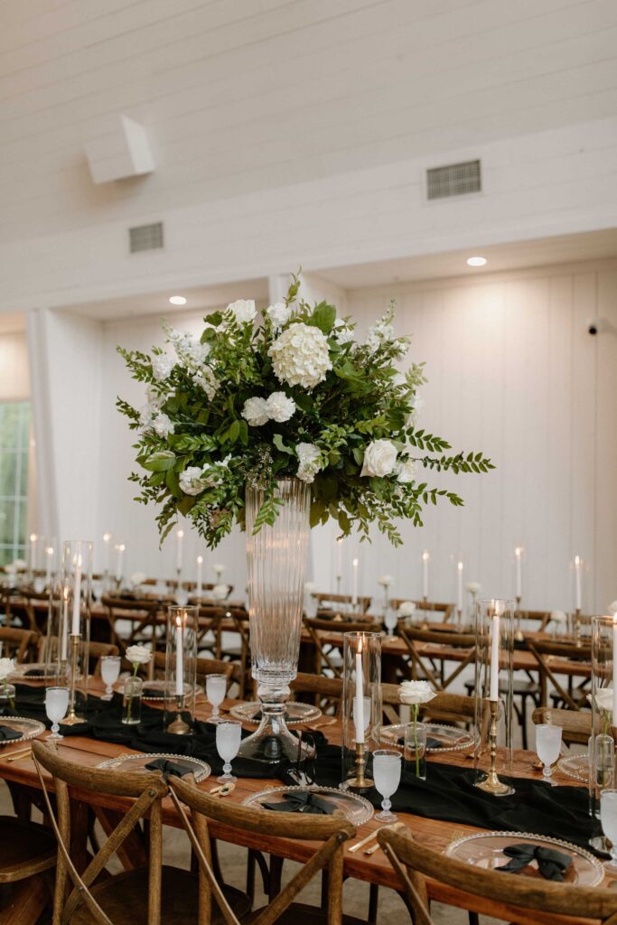 Wedding reception table with a tall white and green floral centerpiece, black linens and candlelight.