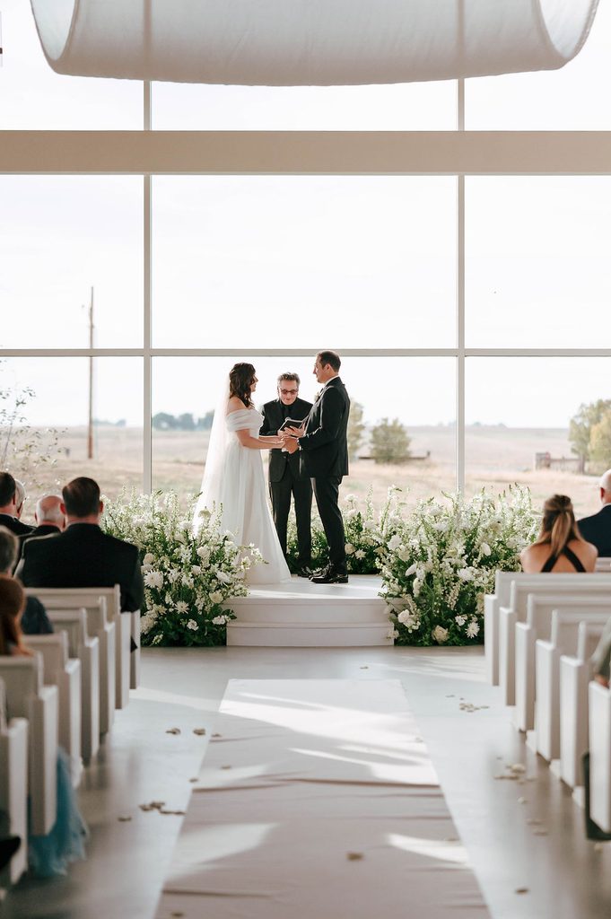 Bride and groom exchanging vows surrounded by lush white and green ceremony florals at Pear Tree Estate.