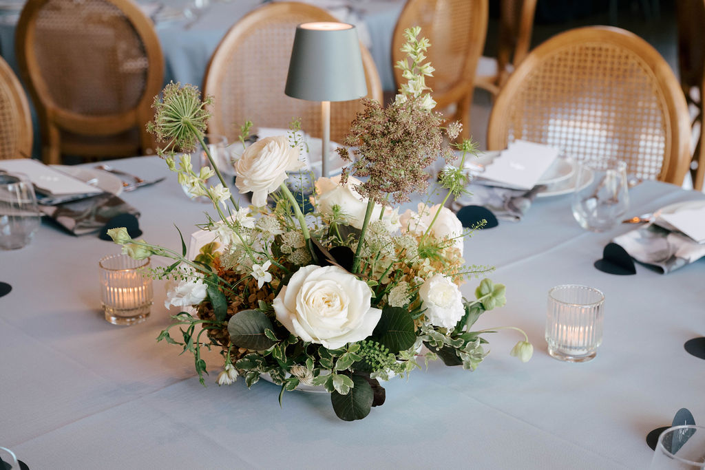 White and green floral centerpiece with roses and textural blooms on a dusty blue reception table at Pear Tree Estate.