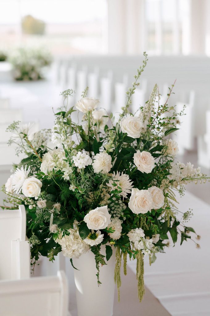 Lush white and green floral arrangement with roses and cascading greenery lining the ceremony aisle at Pear Tree Estate.